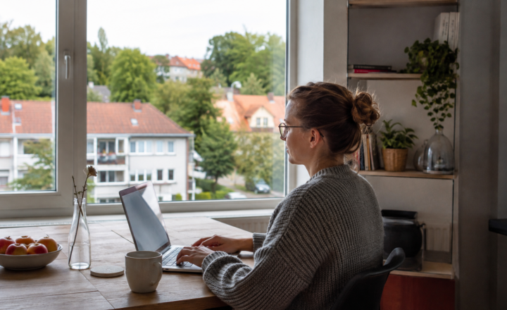 Kobieta pracuje na laptopie przy oknie z widokiem na spokojne osiedle