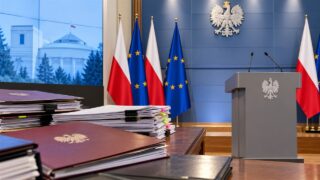 Rządowa sala konferencyjna z dokumentami i flagami Polski oraz Unii Europejskiej