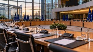 Pusta sala negocjacyjna, stoły, mikrofony i flagi Unii Europejskiej