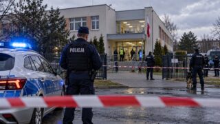Policjanci i radiowóz w pobliżu budynku szkolnego w deszczowy dzień
