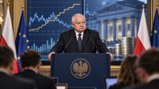 Prezes banku centralnego przemawia przy mównicy, w tle wykres i symbole gospodarki