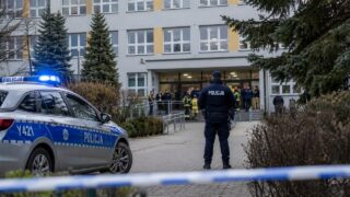 Radiowóz i funkcjonariusz policji przy budynku szkolnym w Polsce