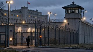 Zabezpieczony zakład karny z wieżą strażniczą i ogrodzeniem pod napiętym niebem