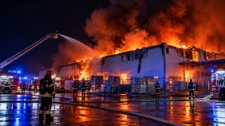 Strażacy gaszą nocą płonącą dużą halę magazynową przy użyciu drabiny i wozów gaśniczych