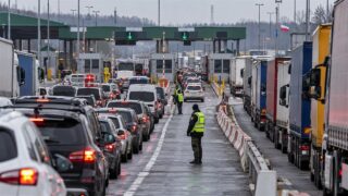 Długi sznur samochodów osobowych i ciężarówek na przejściu granicznym