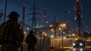 Chroniony obiekt przemysłowy z dronem, ogrodzeniem i służbami bezpieczeństwa nocą