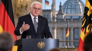 Frank-Walter Steinmeier przy mównicy na tle niemieckich flag