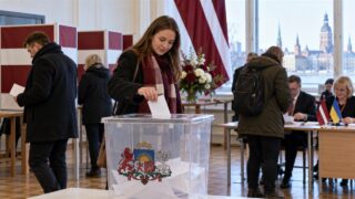 Wyborczyni wrzuca kartę do urny w lokalu wyborczym na Łotwie
